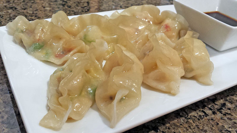 A photograph of freshly made crab meat dumplings on a plate with soy sauce.