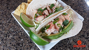 A photograph of crab tacos with Chilean crab meat, avocados, sour cream, green onions, sliced limes and tortilla chips.