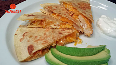 A photograph of a crab quesadilla with sliced avocado and sour cream.