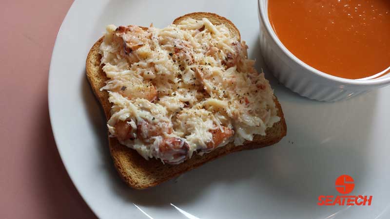 A photograph of crab salad meat on toast with a cup of tomato soup placed next to it.
