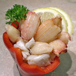 A photograph of Chilean handpicked crab meat in a red bell pepper with  sliced lemon and parsley.