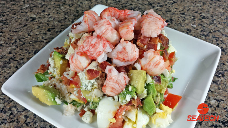A photograph of langostino lobster COBB salad with langositino, boiled eggs, bacon, avocado, blue cheese, tomatos and lettuce