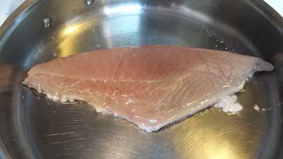 A photograph of a skin on Chilean pomfret fillet cooking skin side down.