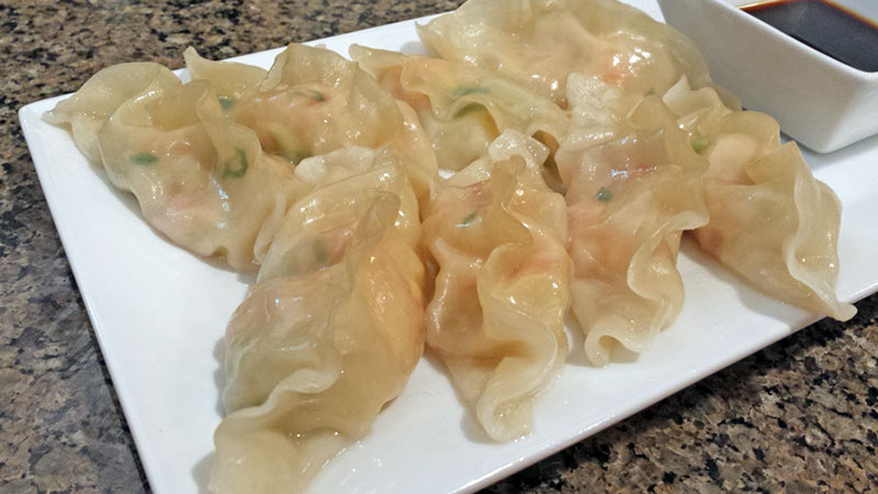 A photograph of freshly made Chilean shrimp dumplings on a plate with soy sauce