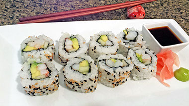 A photograph of freshly made Chilean shrimp sushi roll on a plate with soy sauce, pickled ginger and wasabi.