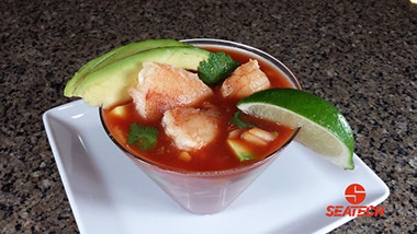 A photograph of a Mexican crab cocktail with tomato juice, crab, onion, avocado, cilantro and lime juice.