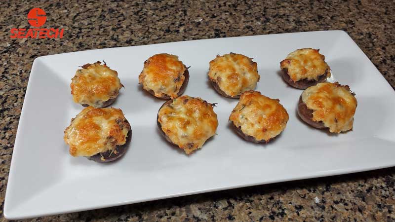 Mushrooms stuffed with crab meat, cheese and chives topped with more cheese and backed.