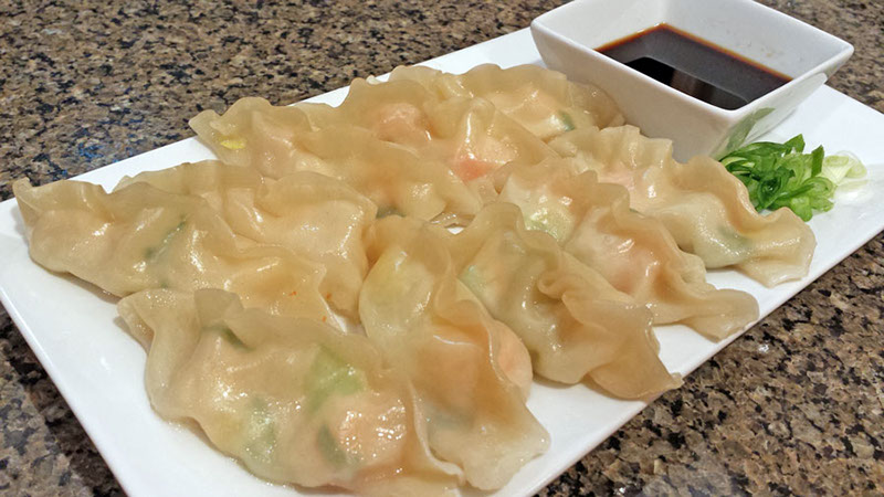 A photograph of freshly made langostino lobster dumplings on a plate with soy sauce and sliced green onions.