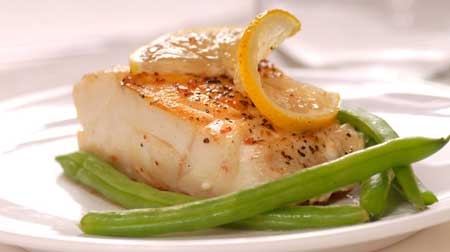 A photograph of a pan seared paiche fillet with herbs and lemon served with green beans.