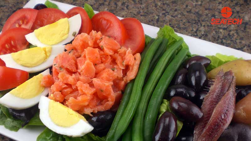 A photograph of salmon tartar nicoise salad with hard boild eggs, green beans, olives, potatoes, anchovies, tomatoes and salmon tartar.