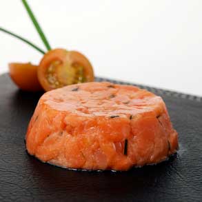 A photorgraph of salmon tartar with a sliced cherry tomato and chives.