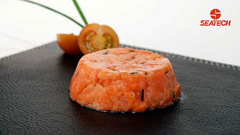 A photograph of salmon tartar with a sliced cherry tomato and chives in the background.